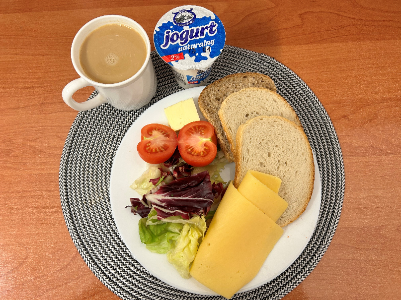 Na zdjęciu znajduje się: Jogurt naturalny, Kawa zbożowa z mlekiem, Chleb mieszany pszenno-żytni, Chleb Graham, Masło extra 82%, Ser żółty, Pomidor, ​​​​​​​Mix sałat